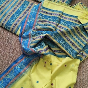May include: A bright yellow fabric set featuring a large piece of cloth with blue and red patterned borders and stripes, accompanied by two folded rectangular pieces of matching fabric. The main cloth has small scattered red and blue square motifs.