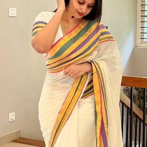 Könnte beinhalten: Ein cremefarbener Sari mit einem breiten Rand aus horizontalen Streifen in den Farben Violett, Grün, Gelb und Pink. Das Kleidungsstück umfasst eine passende Bluse mit kurzen Ärmeln und V-Ausschnitt, die mit demselben bunten Streifenmuster verziert ist.