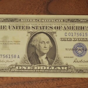 May include: A vintage one-dollar silver certificate from the United States, featuring a portrait of George Washington. The bill has a green seal and serial number C01756158A. The text includes "Silver Certificate" and "One Dollar."