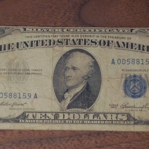 May include: A vintage ten-dollar silver certificate from The United States of America. The bill features a portrait of Alexander Hamilton and the text "TEN DOLLARS" in the center. The bill is in shades of blue and gray.