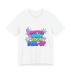 May include: White t-shirt with a colorful graphic that reads "HOTTER THAN YOUR DIAL-UP". The design features a pink flip phone, stars, and a heart. The text is in a mix of blue, green, and pink colors.