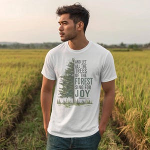 Könnte beinhalten: Ein weißes kurzärmeliges T-Shirt mit einer Grafik eines grünen Nadelbaums auf der linken Seite und dem Text AND LET ALL THE TREES OF THE FOREST SING FOR JOY PSALM 96:12 auf der rechten Seite, mit einer kleinen Waldlandschaft am unteren Rand.