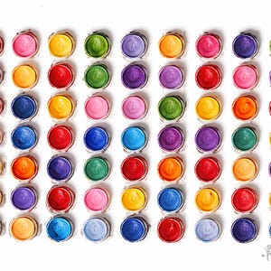 Pu&ograve; includere: Una griglia di settantadue piccoli contenitori circolari riempiti con varie tonalit&agrave; di vernice pigmentata, tra cui rosso, arancione, giallo, verde, blu, viola e rosa, disposti in otto righe e nove colonne su uno sfondo bianco.