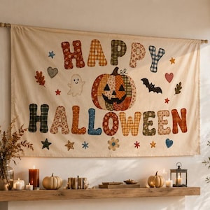 Puede incluir: Un tapiz rectangular de tela con el texto HAPPY HALLOWEEN en letras mayúsculas coloridas y estampadas. El diseño incluye una calabaza central, un fantasma, un murciélago y varias estrellas, corazones y hojas pequeñas sobre un fondo crema.