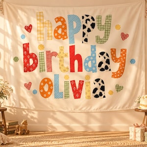 Może przedstawiać: Białe tło z tkaniny z kolorowym napisem "happy birthday Olivia" w r&oacute;żne wzory, w tym kratkę vichy, kwiaty i krowie łaty. Litery ozdobione są małymi sercami i k&oacute;łkami, a baner jest zawieszony na girlandzie z tr&oacute;jkątnych chorągiewek.