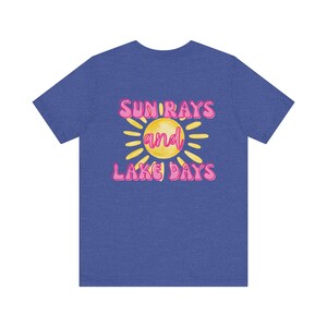Könnte beinhalten: Blaues T-Shirt mit dem Text "SUN RAYS and LAKE DAYS" in Pink und Gelb. Das Design zeigt eine gelbe Sonne mit rosa Strahlen. Das Shirt ist ein Freizeitkleidungsstück.