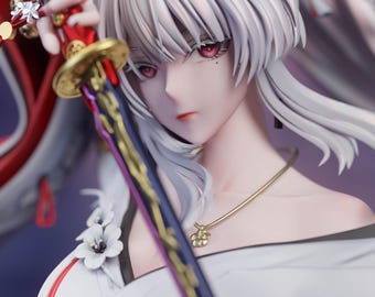 Könnte beinhalten: Eine detaillierte Anime-Figur mit langem weißem Haar und roten Augen, bekleidet mit einem weißen Gewand mit floralen Akzenten. Die Figur hält ein Schwert mit einem rot-goldenen Griff. Der Text unten lautet May 2026 Patreon | Sylviana Sculpt.