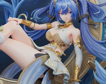 May include: A collectible anime-style figurine featuring a character with long blue hair in twin tails, wearing a white and gold outfit with intricate metallic accents. The figure is posed in a seated position against a circular, ornate gold frame.