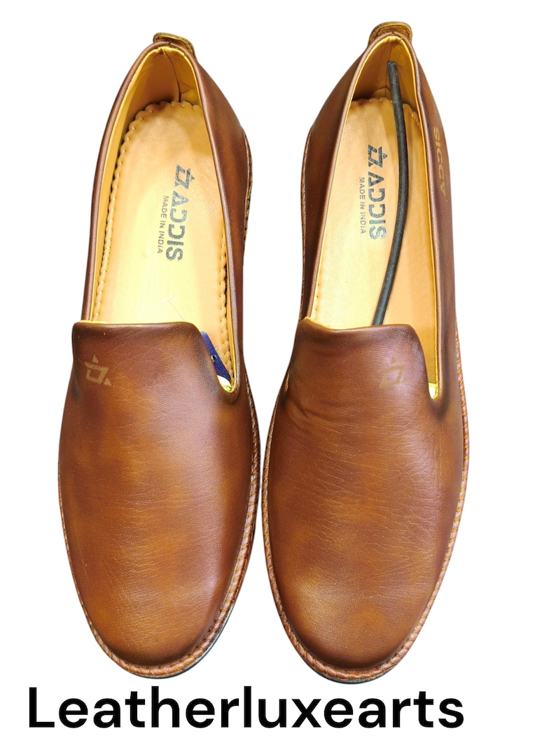 Pu&ograve; includere: Un paio di scarpe slip-on in pelle marrone. Le scarpe hanno la punta arrotondata e la suola cucita. L'interno &egrave; di colore marrone chiaro, con il marchio "ADDIS" visibile. Le scarpe sono esposte su sfondo bianco.