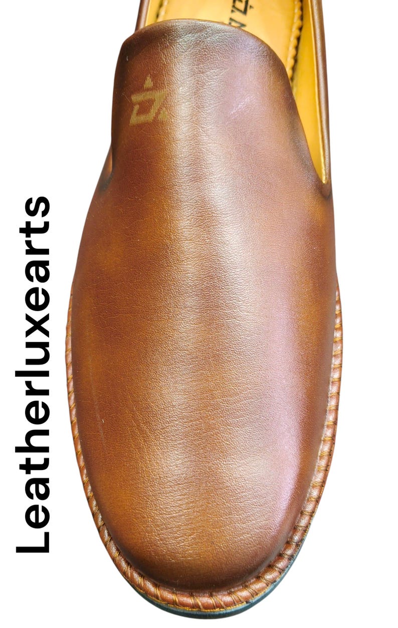 Pu&ograve; includere: Primo piano di una scarpa in pelle marrone. La scarpa ha una punta arrotondata e una suola cucita. La tomaia &egrave; liscia e lucida, con un logo sottile in alto. Il testo "Leatherluxearts" &egrave; stampato verticalmente a sinistra.