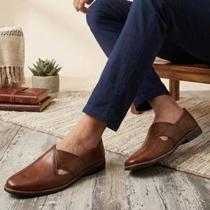 Puede incluir: Zapatos sin cordones de cuero marr&oacute;n con un dise&ntilde;o recortado. Los zapatos tienen una punta puntiaguda y un tac&oacute;n bajo. La persona lleva pantalones azul marino. Los zapatos est&aacute;n sobre un suelo de madera.