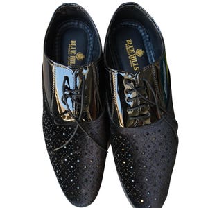 May include: A pair of black dress shoes with a glossy patent leather upper and a perforated suede vamp. The shoes have a lace-up closure and the text "BLUE HILLS PRODUCT OF INDIA" is visible on the insole. The brand name "Leatherluxearts" is at the bottom.