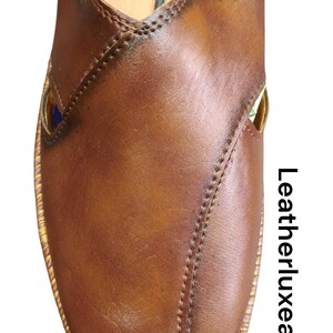 Puede incluir: Primer plano de un zapato de cuero marr&oacute;n con un dise&ntilde;o cosido. El zapato tiene una puntera redondeada y un ribete dorado. El texto "Leatherluxearts" est&aacute; impreso verticalmente en el lado derecho de la imagen. El zapato est&aacute; hecho en India.