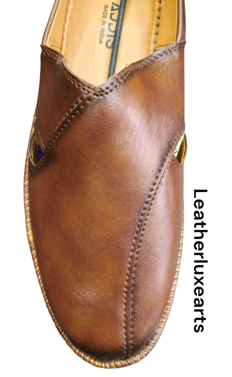 Puede incluir: Primer plano de un zapato de cuero marr&oacute;n con un dise&ntilde;o cosido. El zapato tiene una puntera redondeada y un ribete dorado. El texto "Leatherluxearts" est&aacute; impreso verticalmente en el lado derecho de la imagen. El zapato est&aacute; hecho en India.