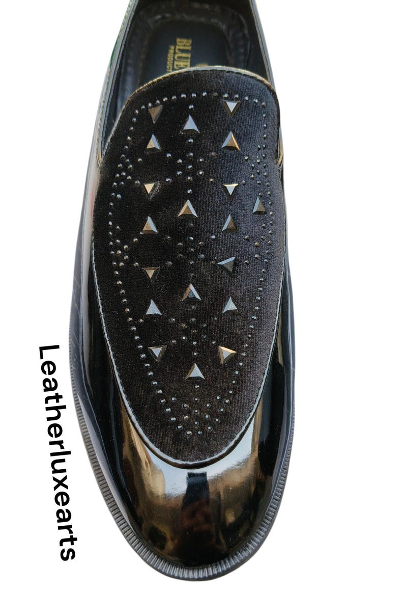 May include: Black patent leather loafer with a velvet vamp. The vamp is decorated with silver-tone triangle studs and small round studs. The shoe has a glossy finish and a rounded toe. The text "Leatherluxearts" is on the side.