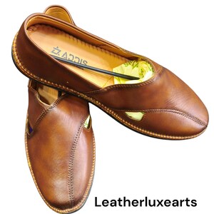 Puede incluir: Un par de zapatos sin cordones de cuero marr&oacute;n con punta y costuras decorativas. Los zapatos tienen un dise&ntilde;o recortado en los laterales y un ribete dorado. La marca "ADDIS" es visible en el interior. El texto "Leatherluxearts" est&aacute; en la parte inferior.