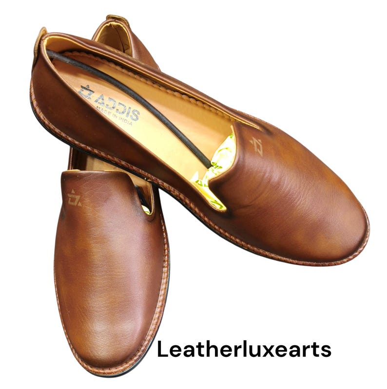 Pu&ograve; includere: Mocassini in pelle marrone dal design classico. Le scarpe hanno una finitura liscia e lucida e una punta arrotondata. Il marchio "ADDIS" &egrave; visibile sul lato. Il testo "Leatherluxearts" &egrave; in basso.