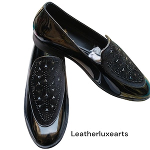 May include: Pair of black patent leather loafers with a velvet vamp embellished with silver-tone studs. The shoes have a sleek, glossy finish and a low heel. The text "Leatherluxearts" is visible.