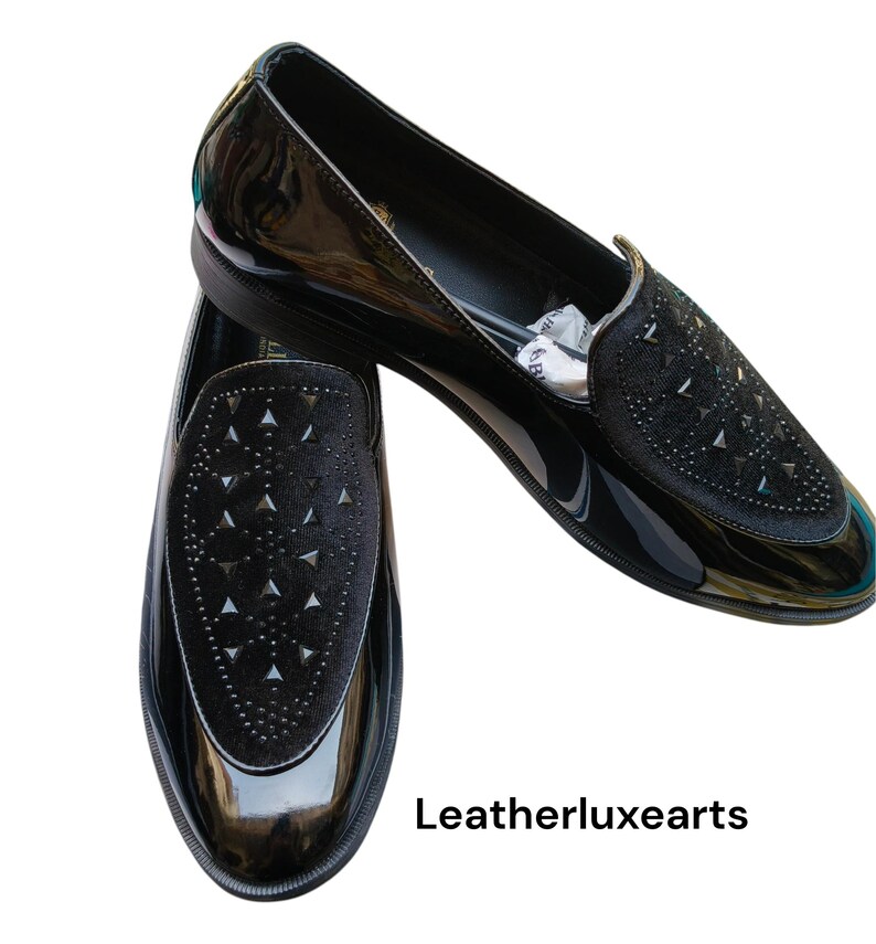 May include: Pair of black patent leather loafers with a velvet vamp embellished with silver-tone studs. The shoes have a sleek, glossy finish and a low heel. The text "Leatherluxearts" is visible.