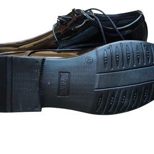 May include: Pair of glossy black dress shoes with laces. One shoe is upright, the other is upside down, revealing the textured sole. The shoes have a classic design, suitable for formal occasions.