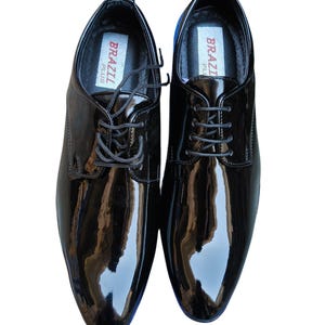 May include: A pair of glossy black leather dress shoes with laces. The shoes have a polished finish and a classic design. The insoles are labeled "BRAZIL PLUS". The image also includes the text "Leatherluxearts".