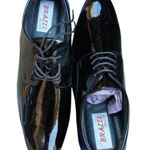 May include: Pair of glossy black dress shoes with laces. The shoes have a shiny patent leather finish and the brand name "BRAZIL PLUS" is visible inside. The text "Leatherluxearts" is at the top.
