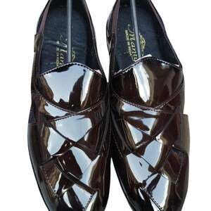 May include: A pair of dark brown, high-gloss loafers featuring a woven-style upper design. The interior of the shoes displays a black insole with the text "Many" and "MADE IN INDIA" printed in gold. The brand name "Leatherluxearts" appears below.