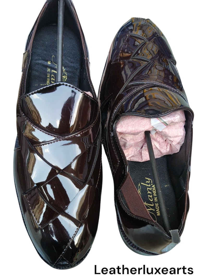 May include: A pair of dark brown loafers with a high-gloss patent finish. The upper features a woven-style overlapping strap design. The interior of the shoe is black with the text "Manly" and "MADE IN INDIA" printed on the insole.
