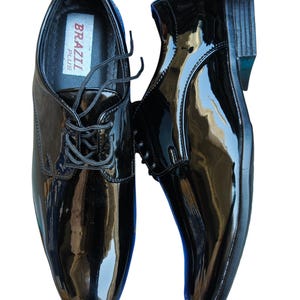 May include: Pair of glossy black dress shoes with laces. The shoes have a shiny patent leather finish and a classic design. The brand name "BRAZIL PLUS" is visible inside one shoe. The shoes are displayed on a white background.