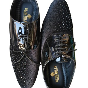 May include: A pair of black dress shoes with a glossy patent leather vamp and a textured, studded design on the toe box. The shoes have laces and the text "BLUE HILLS PRODUCT OF INDIA" is visible on the insole.