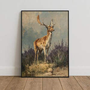 May include: A framed wall art print featuring an oil painting of a fallow deer standing in a field of tall grass and purple heather. The deer has a light brown coat with white spots and large antlers, set against a soft blue and cloudy sky.