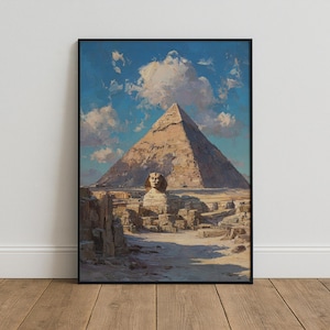 May include: A framed wall art print depicting the Great Pyramid of Giza and the Great Sphinx of Giza under a bright blue sky with scattered white clouds. The scene features sandy desert terrain, rocky foreground elements, and warm sunlight.
