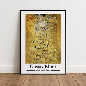 Puede incluir: Impresión artística enmarcada de "Adele Bloch-Bauer I" de Gustav Klimt. La obra presenta un retrato de una mujer con un vestido dorado con patrones intrincados. La impresión está en un marco negro, con el nombre del artista y el título de la obra en la parte inferior.