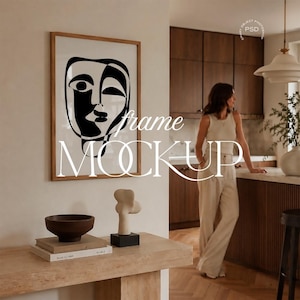 May include: A framed art print featuring a black and white abstract face design. The artwork is displayed in a light brown wooden frame. The image also shows a wooden console table with decorative items, including a bowl and a sculpture.