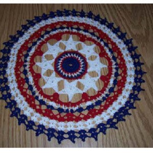 May include: A handmade, circular doily in red, white, and blue crochet. The doily features a starburst pattern in the center, with concentric rings of color and a scalloped edge. The diameter is approximately 10 inches.