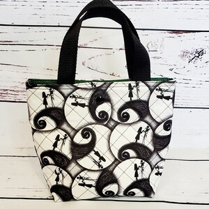 May include: A small black and white tote bag with a quilted design. The bag features a repeating pattern of silhouettes of Jack Skellington and Sally from the Nightmare Before Christmas movie. The bag has black handles.