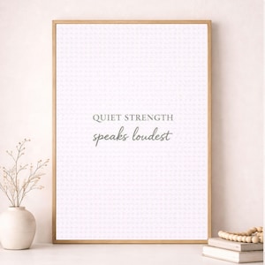 Può includere: Una stampa incorniciata con le parole "QUIET STRENGTH speaks loudest" in un carattere grigio chiaro. Lo sfondo presenta un motivo strutturato e sottile. La cornice è in legno chiaro. Un vaso bianco con fiori secchi a sinistra.