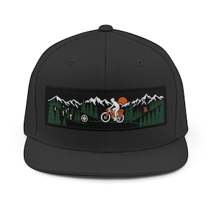 Pode incluir: Boné preto de aba reta com um patch retangular com uma cena de mountain bike. O patch mostra um ciclista em uma mountain bike, árvores, montanhas e um sol poente. O boné é de cor preta lisa.