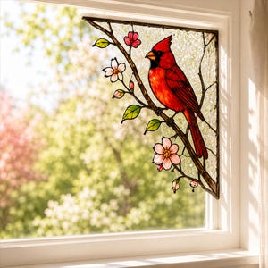 May include: Stained glass window panel featuring a vibrant red cardinal perched on a branch with pink blossoms and green leaves. The artwork is framed in a dark brown border, creating a decorative accent for any window.