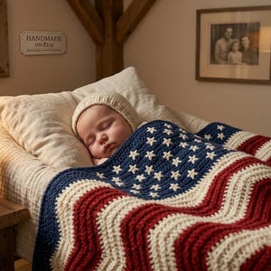 May include: A sleeping baby wearing a knit cap is covered with a red, white, and blue crocheted blanket with a star and stripe design. A small teddy bear and wooden toys are in a basket on a wooden table. The sign on the wall says "Handmade on Etsy."