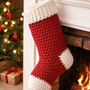 May include: A handmade Christmas stocking in red and white crochet. The stocking is hanging on a white mantelpiece with a gift box and Christmas tree in the background. The stocking has a white cuff and toe.