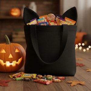 Peut inclure: Un sac fourre-tout noir avec des oreilles de chat rempli de bonbons assortis, une citrouille sculptée avec un visage éclairé et des bonbons et des feuilles éparpillés sur une surface en bois. Thème d'Halloween.