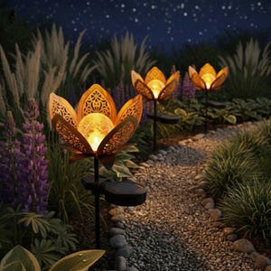 Könnte beinhalten: Solarbetriebene Gartenleuchten in Form von Lotusblumen. Die Leuchten strahlen ein warmes, goldenes Licht aus und sind entlang eines Steinwegs angeordnet. Die Blütenblätter weisen aufwendige Ausschnitte auf. Die Leuchten sind von Grün und lila Blumen umgeben.