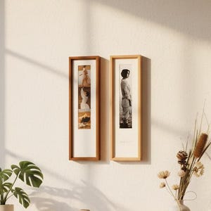 May include: A modern living room scene featuring a light wood console table with a Monstera plant in a white and brown pot. Two framed pictures hang on the wall. A vase with dried flowers and a chair with a blanket complete the decor.