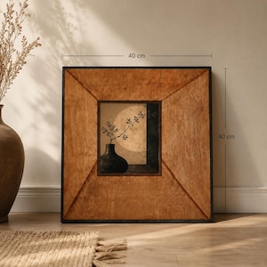 May include: A square wall art piece featuring a dark vase with a leafy branch against a circular moon background, framed in light brown wood with diagonal corner accents. The artwork measures 40 cm by 40 cm as indicated by the visible labels.