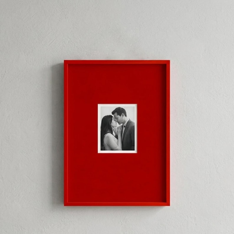 Op de afbeelding: Een vierkante, rode fotolijst met een zwart-witfoto van een kussend stel. De lijst is effen rood van kleur en de foto is gecentreerd in de lijst.