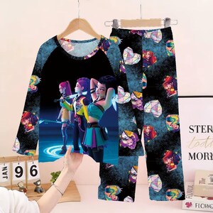 May include: A two-piece pajama set featuring a long-sleeved top and pants. The top has a black raglan sleeve design with a graphic of three animated figures. The pants and sleeves have a repeating pattern of geometric shapes and animated figures.