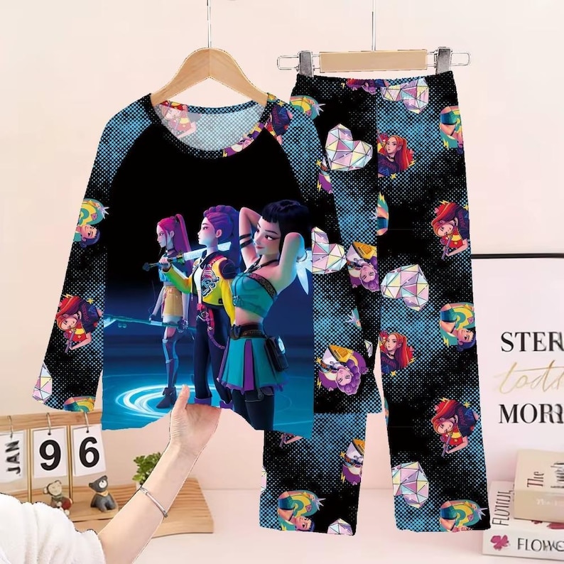 May include: A two-piece pajama set featuring a long-sleeved top and pants. The top has a black raglan sleeve design with a graphic of three animated figures. The pants and sleeves have a repeating pattern of geometric shapes and animated figures.