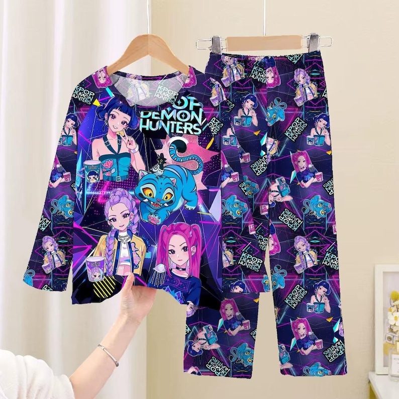 May include: A long-sleeved pajama set featuring a vibrant graphic design. The top and pants are covered in illustrations of anime-style characters, a blue tiger, and the text "OF DEMON HUNTERS" in white. The set is primarily purple with neon accents.