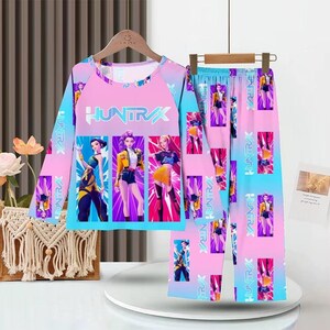 May include: A two-piece pajama set featuring a long-sleeved top and pants. The set is predominantly pink and blue with a repeating graphic of stylized figures. The top displays the word "HUNTRAX".